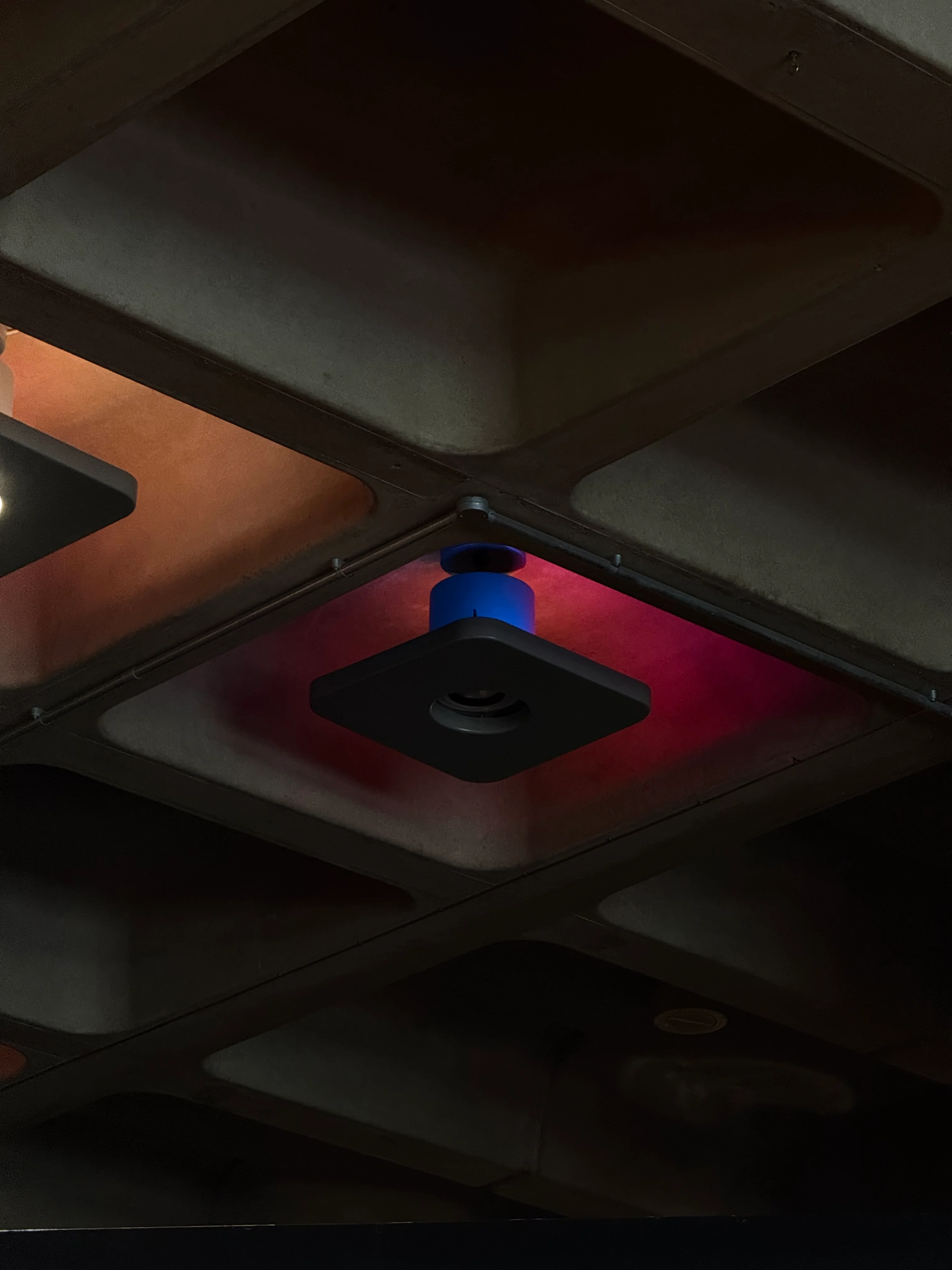 Coloured light illuminating a coffered concrete ceiling.
