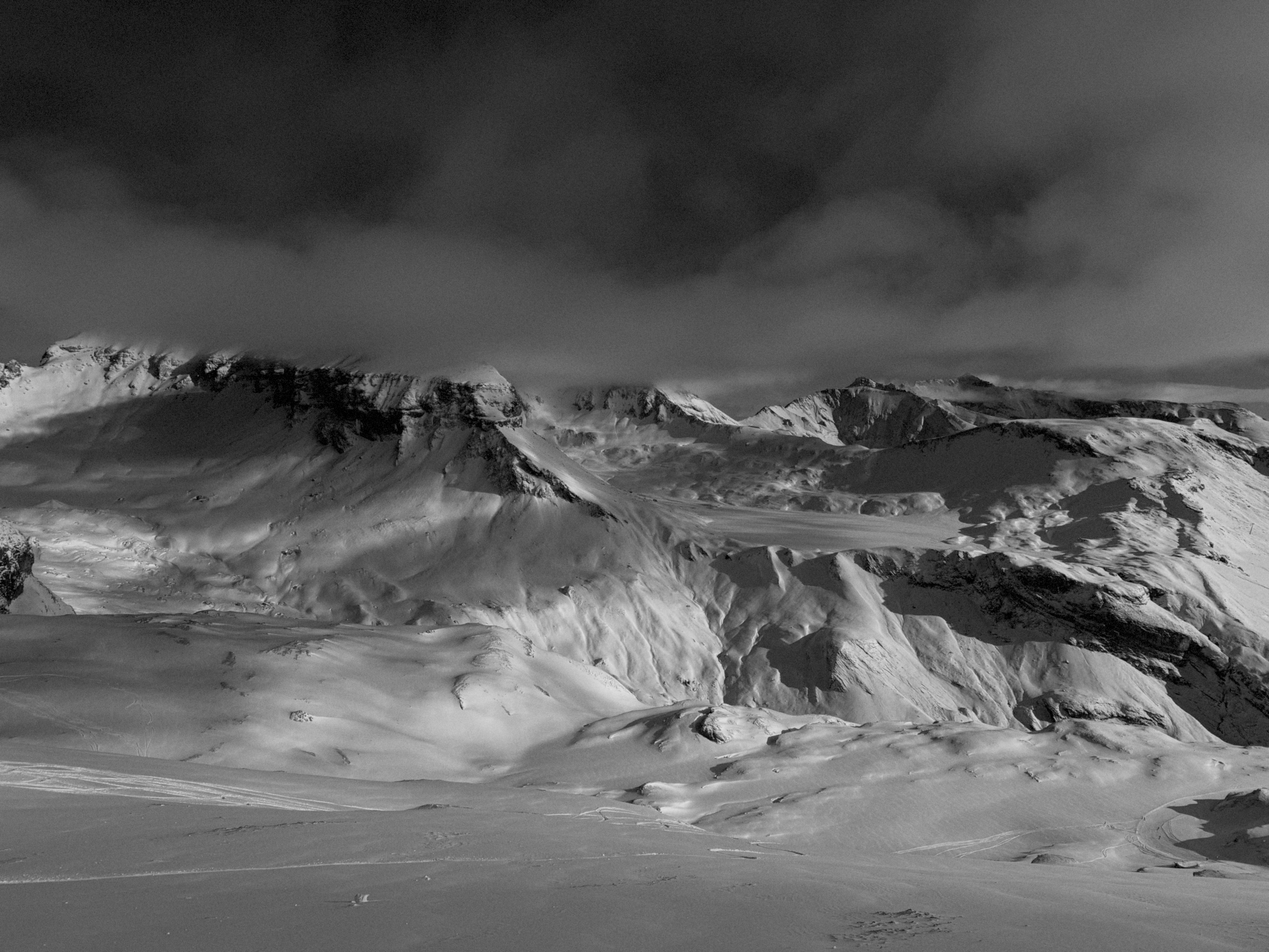 Black-and-white photograph of snow-covered mountains beneath dark clouds.
